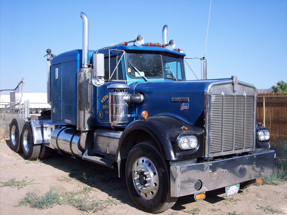 Blue Kenworth W900 semi truck tractor with sleeper cab in a dirt lot