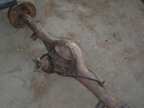 1990 Ford Bronco - A rusty rear axle assembly lies on the ground, likely a component from a vintage vehicle.