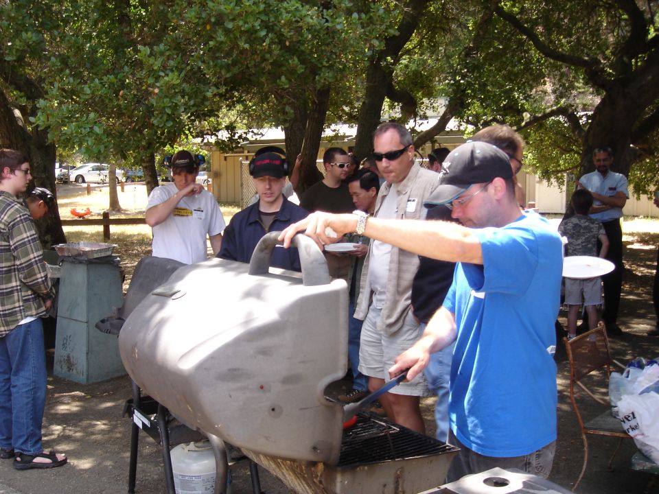 People at an outdoor barbecue with a large grill in the foreground
