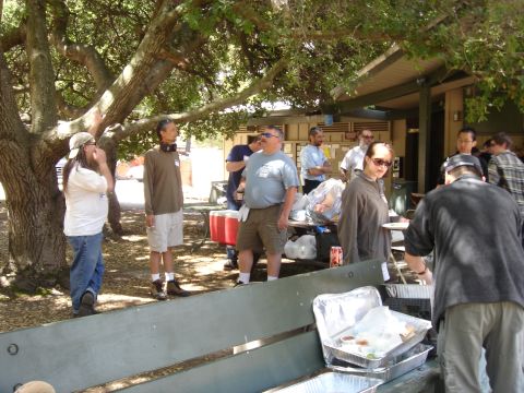 1990 Ford Bronco - People gather outdoors under trees, with food containers visible in the foreground.