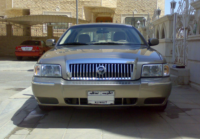 Gold Mercury Grand Marquis, front view, chrome grille, Kuwait license plate, parked in driveway