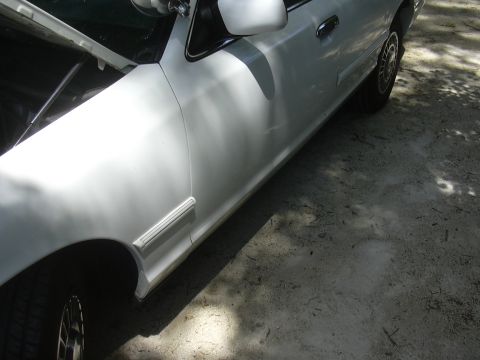 1997 Ford Crown Victoria - The side of a white sedan is visible, with the hood propped open, revealing the engine bay.