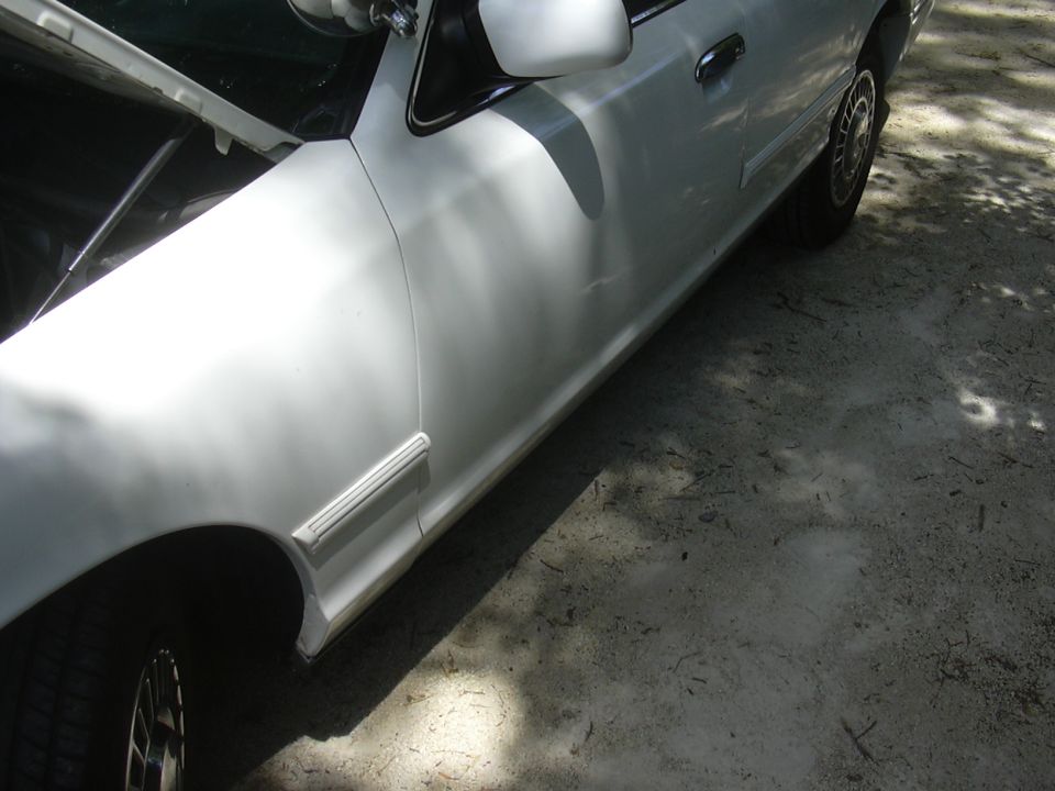 Side view of a white sedan with the hood open. Shows the front fender, door, and side trim