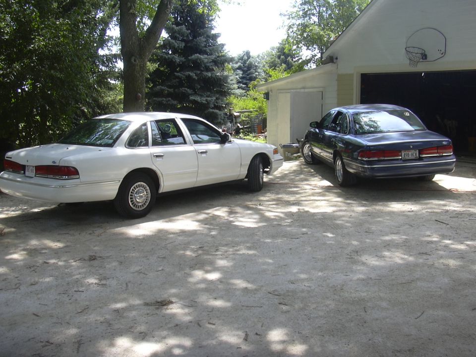 White 1997 Ford Crown Victoria parked next to a dark blue 1997 Ford Crown Victoria in a driveway