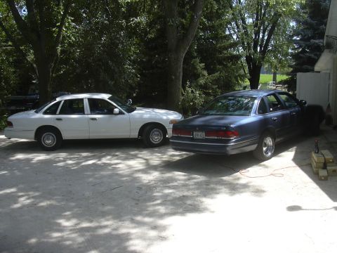 1997 Ford Crown Victoria - A white 1997 Ford Crown Victoria is parked next to a blue sedan in a residential driveway.