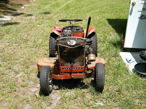 1986 Ford Bronco - This riding lawn mower is parked on a grassy area next to a white door.