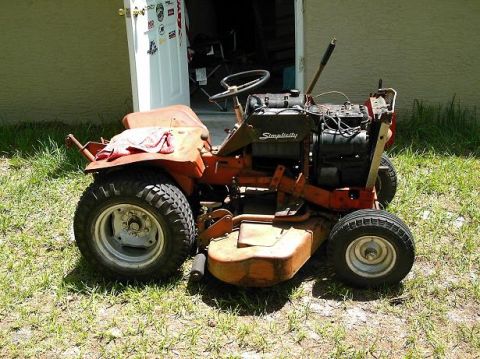 1986 Ford Bronco - This Simplicity riding mower is seen from a three-quarter front view, parked on a grassy lawn in front of a building.
