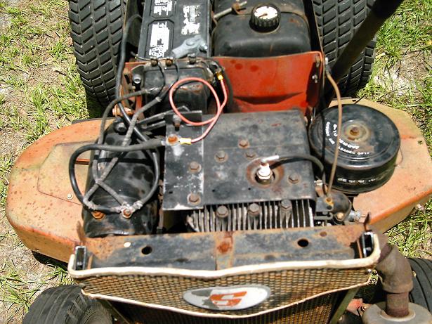 Rusty lawn mower engine with battery, air filter, and spark plug visible