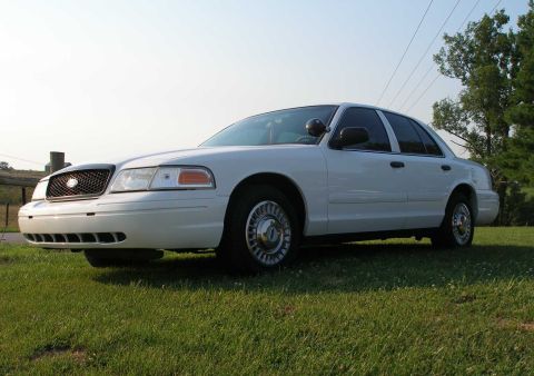2001 Ford Crown Victoria - White 2001 Ford Crown Victoria parked on a grassy area with trees in the background.