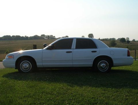 2001 Ford Crown Victoria - A white sedan is shown from the side, parked on a grassy area with a rural landscape behind it.