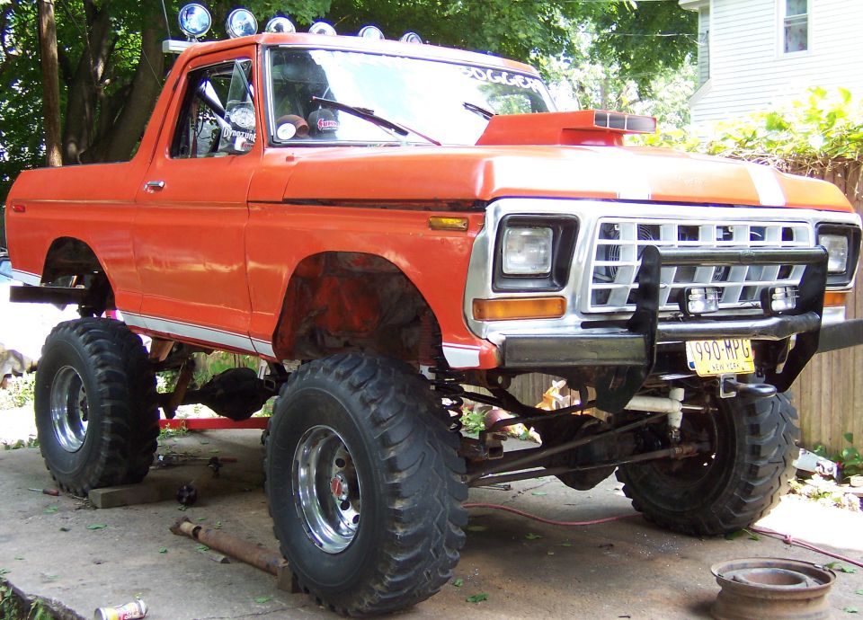 Orange 1978 Ford Bronco with large off-road tires, a hood scoop, and a front brush guard