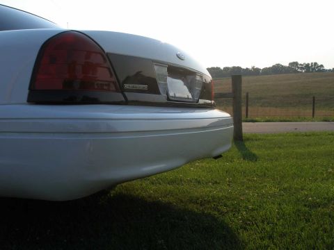 2001 Ford Crown Victoria - Rear view of a white 2001 Ford Crown Victoria parked on a grassy area next to a fence.