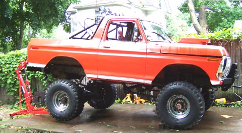 1978 Ford Bronco - A modified 1978 Ford Bronco sits outside, elevated by a hoist and large off-road tires.
