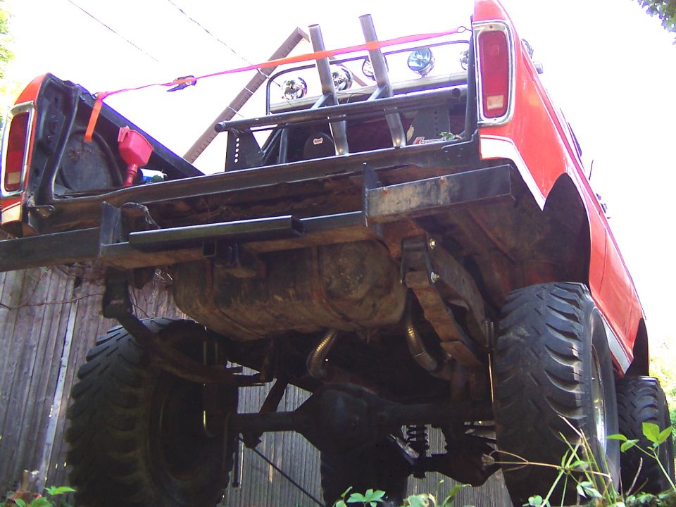 Rear view of a lifted red pickup truck with large tires, custom bumper, and spare fuel can in the bed