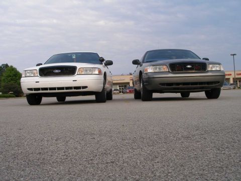 2001 Ford Crown Victoria - Two Ford Crown Victorias are parked side-by-side in a parking lot under a cloudy sky.