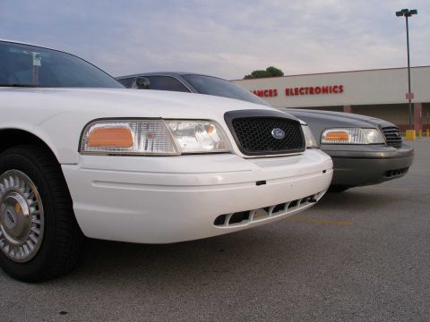 2001 Ford Crown Victoria - Two Ford Crown Victorias are parked outside a store with 'ANCES ELECTRONICS' visible on the building.
