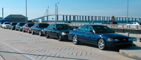 1997 Ford Crown Victoria - Several Ford Crown Victorias are lined up on a bridge with a large body of water in the background.