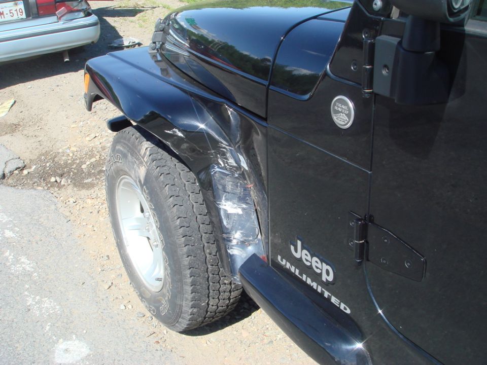 black Jeep Wrangler with dented fender and door, other car in background