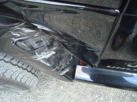 1996 Ford Bronco - The rear quarter panel of a black SUV shows extensive damage, with a tire visible in the foreground.