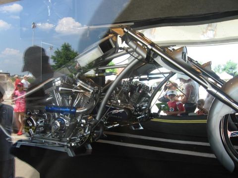 1988 Ford Bronco - A custom motorcycle with a prominent dual-engine setup is displayed indoors, with people observing.