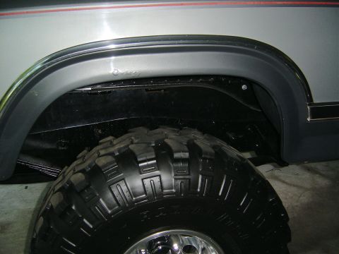 1986 Ford Bronco - Close-up of a white truck body's rear wheel opening with a black fender flare fitted over the lip, showing the cleaned and painted inner wh…
