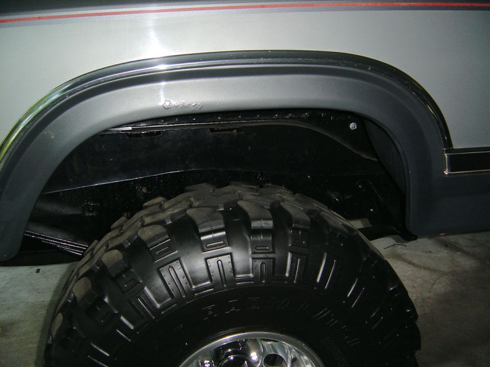 Black fender flare on white truck rear wheel opening over mud-terrain tire