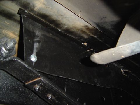 1986 Ford Bronco - Dark close-up of a fabricated black sheetmetal bracket or filler panel held in place against a body panel with a single sheet-metal screw,…