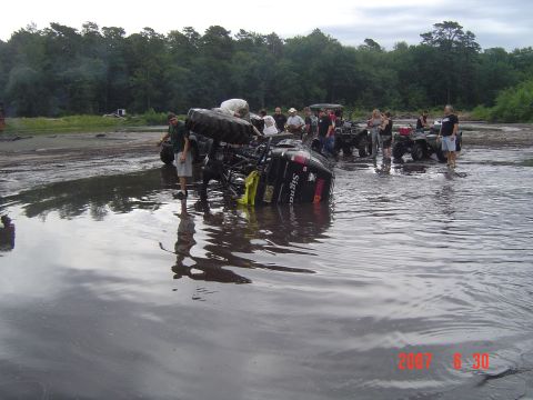 2005 Dodge 1500 - A group of people gather around an overturned ATV in a muddy, watery area. Other ATVs are visible in the background.