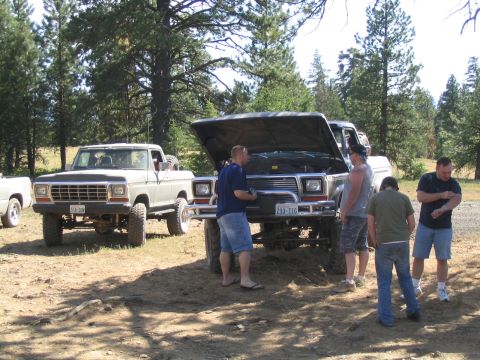 1979 Ford Bronco - Two off-road vehicles are parked in a wooded area, with several people gathered around the Jeep.