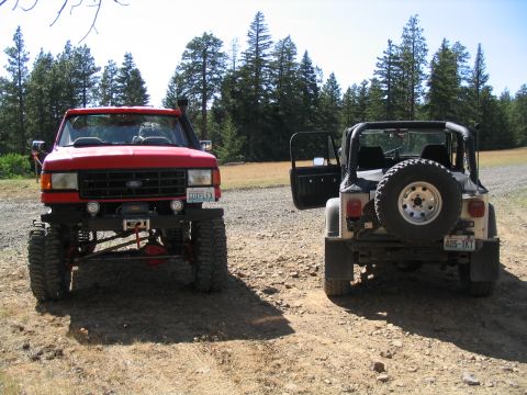 1979 Ford Bronco - A lifted red Ford truck with a snorkel and winch is parked on a dirt road, with a Jeep visible to its right.