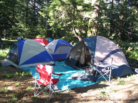 1979 Ford Bronco - A campsite is established with multiple tents and chairs spread across a blue tarp in a wooded area.