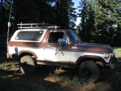 1979 Ford Bronco - This two-tone Ford Bronco is parked on a dirt path surrounded by trees.
