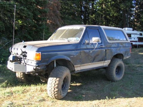 1979 Ford Bronco - A lifted Ford Bronco sits parked outdoors with trees and a camper in the background.