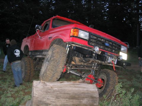 1979 Ford Bronco - A heavily modified red Ford truck navigates an obstacle during an outdoor event.