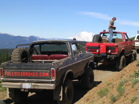 1979 Ford Bronco - Several off-road vehicles, including a black Ford Bronco, are parked on a dirt road with mountains in the background.