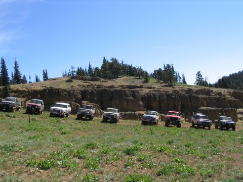 1979 Ford Bronco - A group of off-road vehicles are lined up on a hillside under a clear blue sky.
