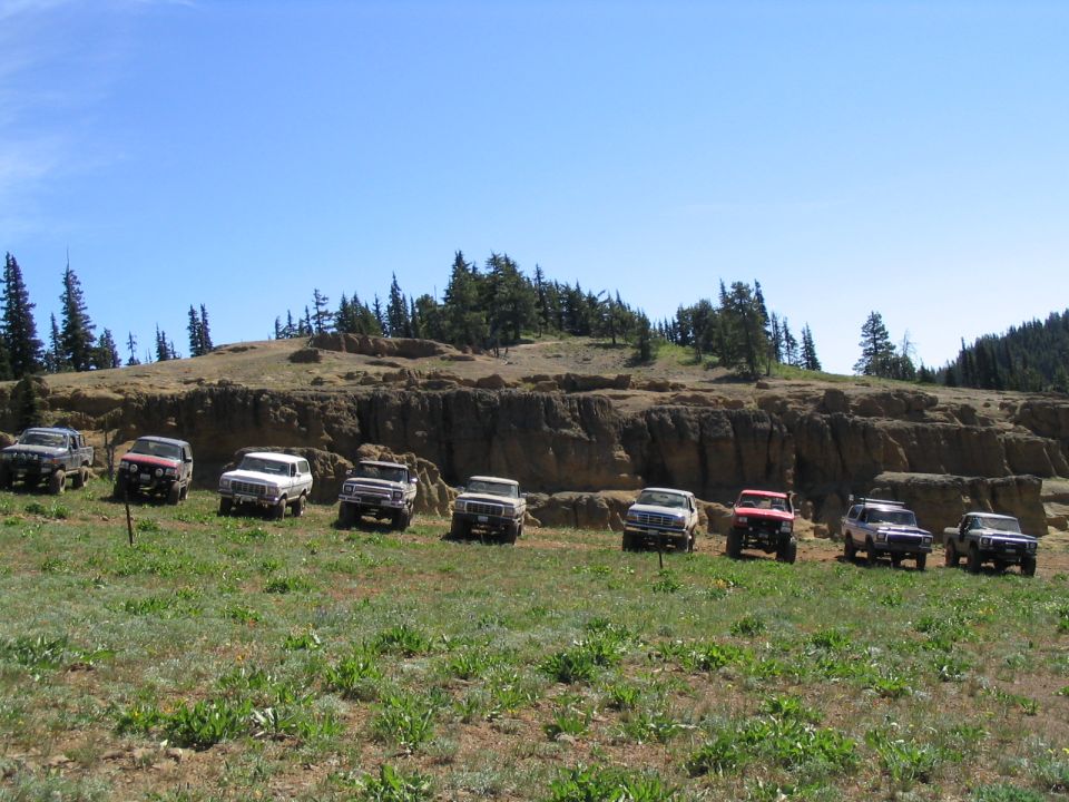 Several off-road SUVs parked in a line on a grassy hill with a rocky cliff face behind them