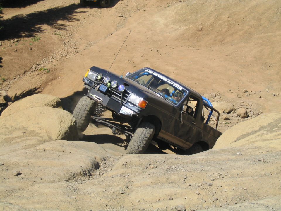 Black off-road truck climbing a steep dirt hill, with another vehicle visible in the background