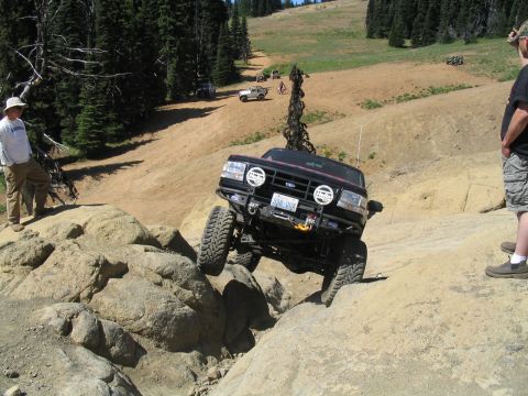 1979 Ford Bronco - A black SUV navigates a challenging rocky trail, with other vehicles visible in the background.
