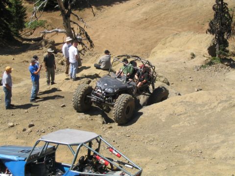 1979 Ford Bronco - Two off-road vehicles are seen on a dusty, rocky terrain with several spectators.