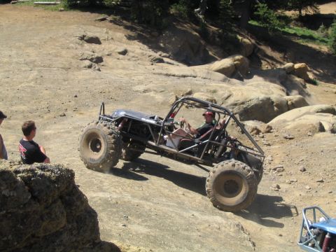 1979 Ford Bronco - An off-road buggy navigates a steep, rocky trail with spectators watching.
