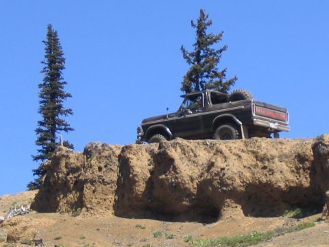 1979 Ford Bronco - A black Ford Bronco is parked on a dirt cliff under a clear blue sky.