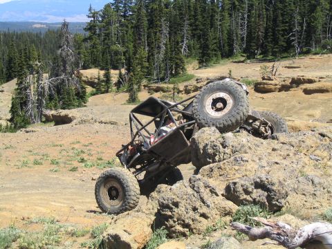 1979 Ford Bronco - A tube-chassis rock buggy climbs a rock ledge at a high-elevation trail area, front end pitched up with the driver's-side front tire hangin…