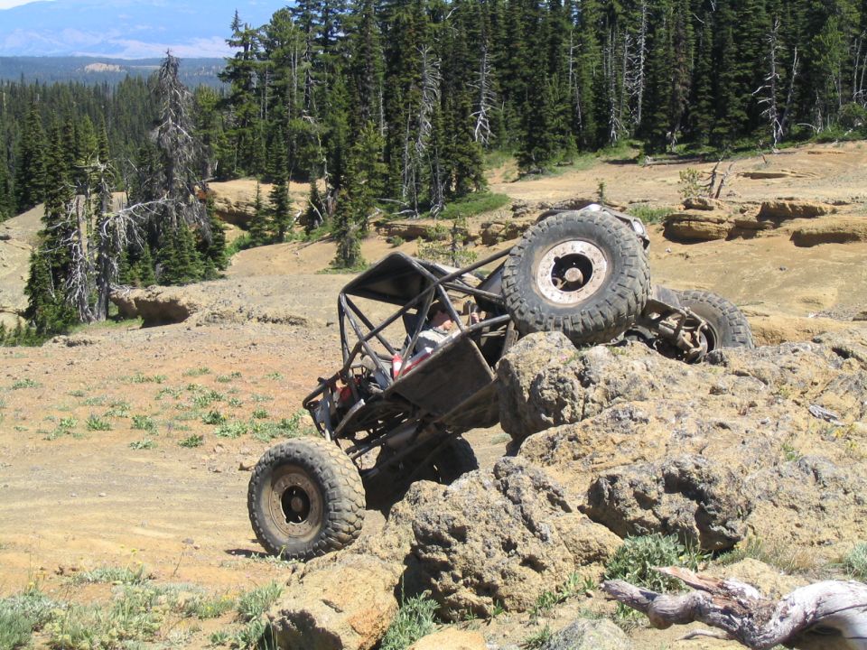 Tube-frame rock buggy on oversized tires climbing a rock ledge on a mountain trail