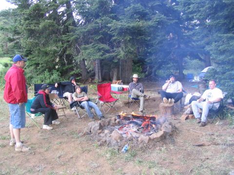 1979 Ford Bronco - A group of people enjoy a campfire in a wooded area, with chairs set up around the fire pit.