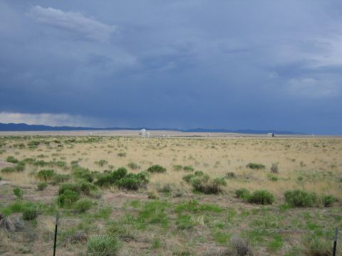 1999 Ford F-250 - Wide view of a desert plain with scattered vegetation and distant scientific structures under a dramatic, cloudy sky.