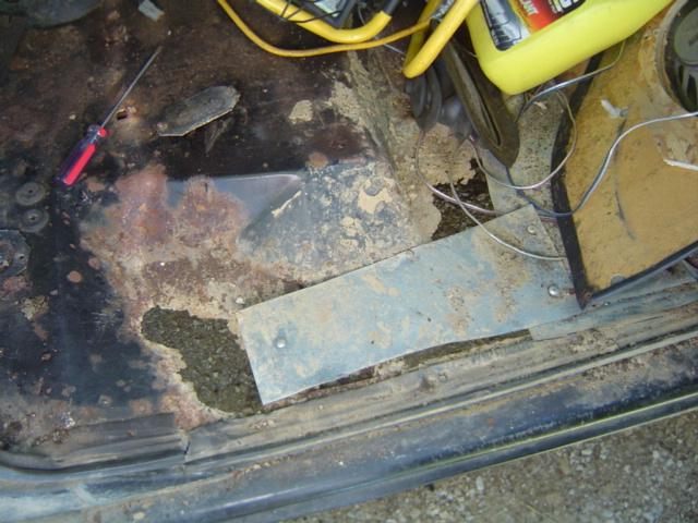 Rusted interior floor pan with a hole, a screwdriver, and a yellow container