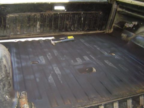 1979 Ford Bronco - The interior cargo area of a vehicle shows a ribbed wall panel and a black floor with some wear. A hammer is visible on the floor.