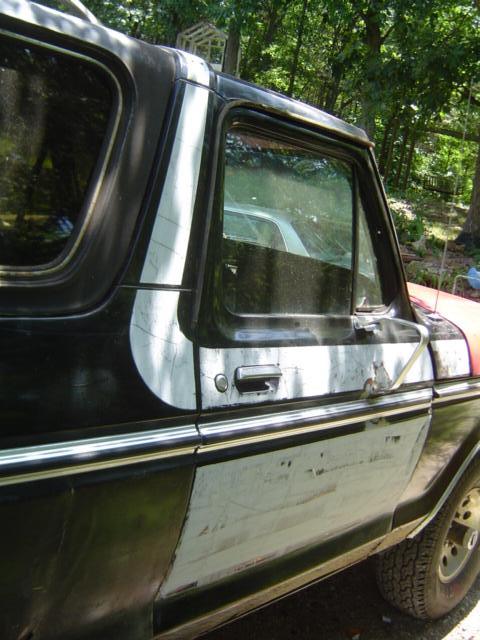 1979 Ford Bronco - Close side view of a Ford Bronco's passenger door and removable hardtop, with the door window down, chrome-trimmed frame, and paint strippe…
