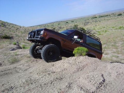 1986 Ford Bronco II - Brown SUV with roof rack navigating a dirt hill with a lifted suspension and off-road tires.